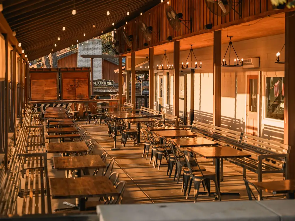 A long covered wooden patio set with tables in golden evening light